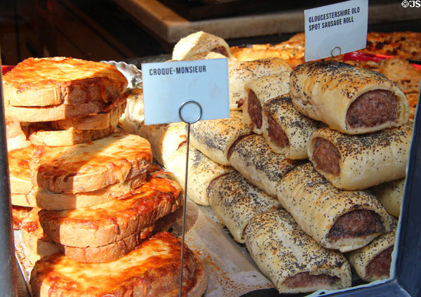 Croque-Monsieur melted cheese sandwiches & sausage rolls in shop window. Cirencester, England.