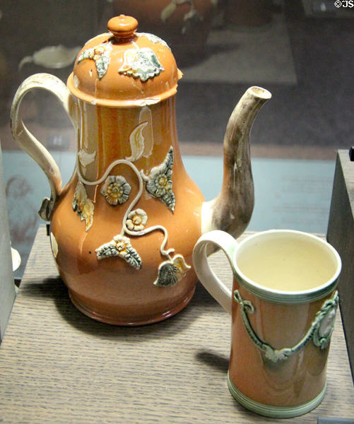 Ochre stained coffee pot & cup with applied molded relief decoration (1750-70) from Staffordshire at Potteries Museum & Art Gallery. Hanley, Stoke-on-Trent, England.