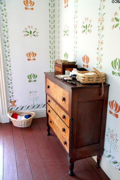 Two tone chest with spiral posts against red & green antique wallpaper pattern in Jonathan Goldsmith House at Hale Farm. Cleveland, OH.