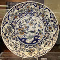Ceramic shallow bowl with center decoration of Chinese style bird on a rock & on-rim medallions of Christian symbol of three entwined fish, likely made in Bristol, at Bristol Museum & Art Gallery. Bristol, England.
